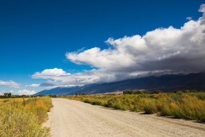 image of dirt road with mountains and clouds