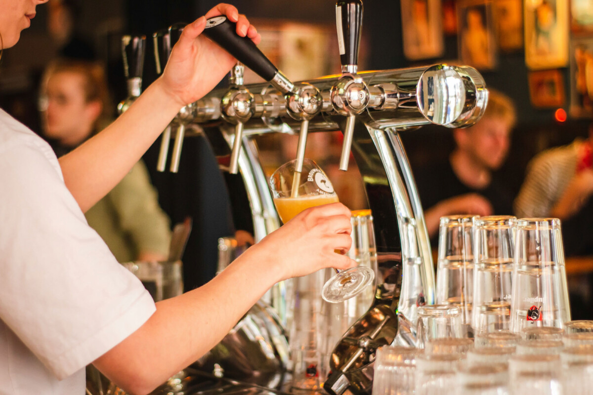 Bartender pouring draft beer into a glass from a tap in a busy bar in Bishop, California. Glasses are stacked nearby on the counter, reflecting the charm of the Eastern Sierra. visit bishop