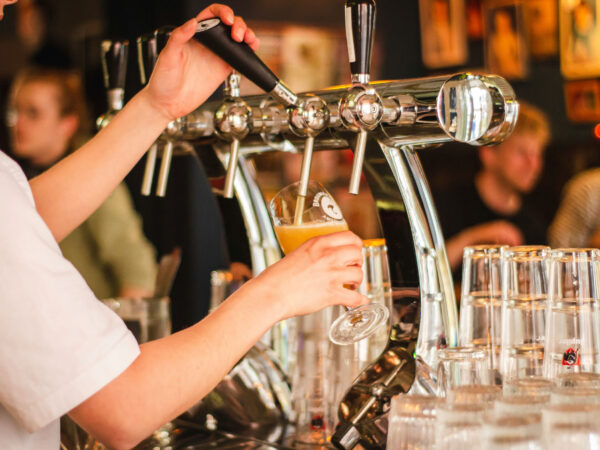 Bartender pouring draft beer into a glass from a tap in a busy bar in Bishop, California. Glasses are stacked nearby on the counter, reflecting the charm of the Eastern Sierra. visit bishop