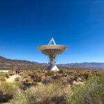 A large satellite dish under clear blue skies in a desert landscape with mountains in the background. visit bishop