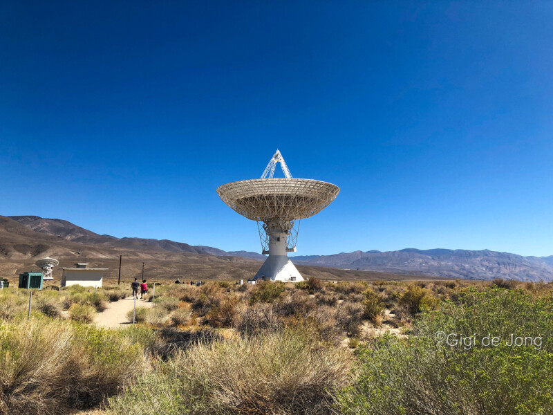 A large satellite dish under clear blue skies in a desert landscape with mountains in the background. visit bishop