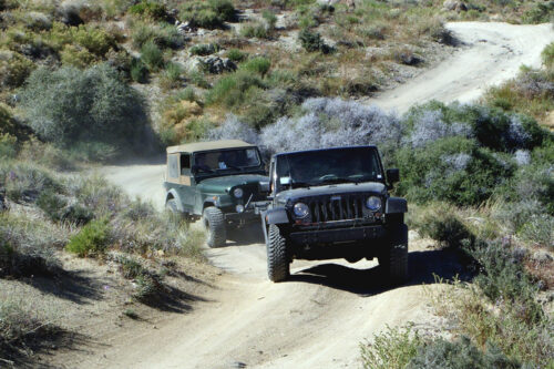 Two jeeps driving on a rugged dirt trail through a mountainous desert landscape under clear skies. visit bishop