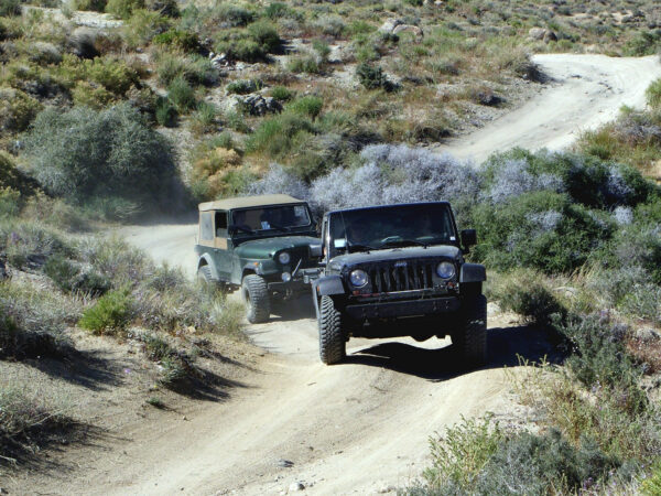 Two jeeps driving on a rugged dirt trail through a mountainous desert landscape under clear skies. visit bishop