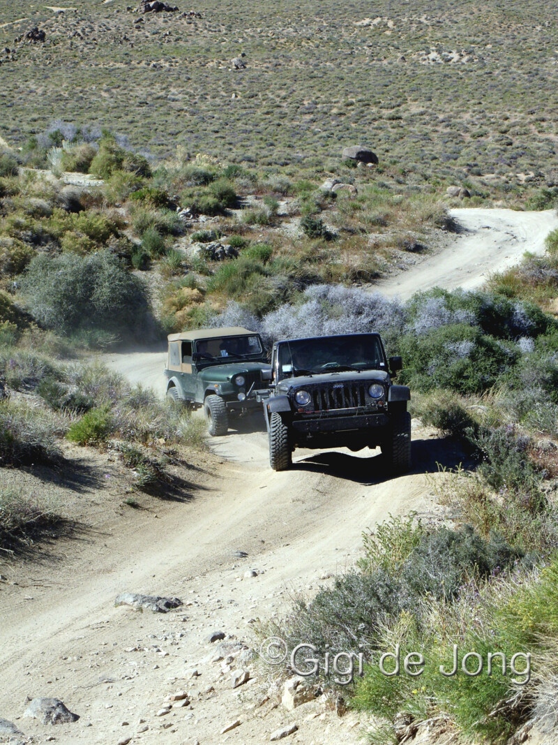 Two jeeps driving on a rugged dirt trail through a mountainous desert landscape under clear skies. visit bishop