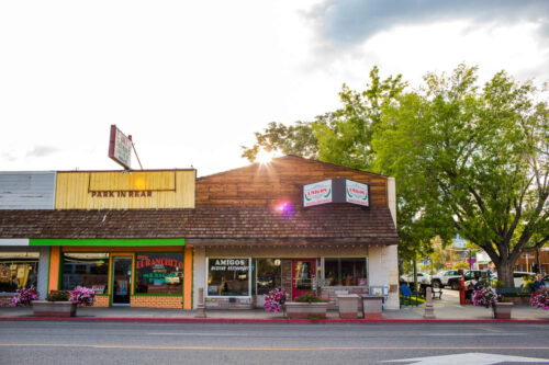 Street view of local businesses in Bishop, California, including El Ranchito, Amigos, and Leona's with trees and flowers from the Eastern Sierra in the background. visit bishop