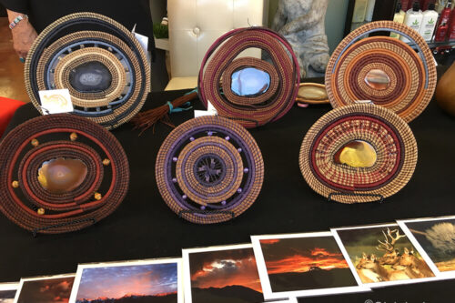 A display of woven baskets with stones at the center, alongside nature photographs. Photographer credit: Gigi de Jong. visit bishop