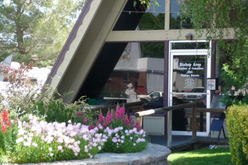 A building entrance with a sign for "Bishop Area Chamber of Commerce and Visitors Bureau," surrounded by colorful flowers. visit bishop