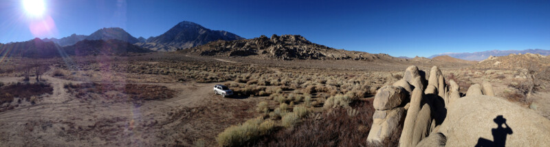 Panoramic view of a dry, rocky landscape with a white car parked in the middle. Mountains are visible in the background. visit bishop