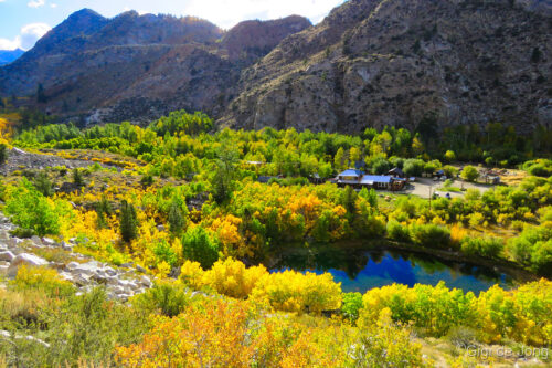 Scenic view of a small lakeside village surrounded by lush autumn trees and mountainous terrain under a partly cloudy sky. visit bishop