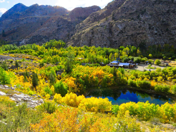 Scenic view of a small lakeside village surrounded by lush autumn trees and mountainous terrain under a partly cloudy sky. visit bishop