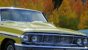 A vintage yellow car with a shiny hood stands proudly against a backdrop of vibrant autumn trees, evoking the charm of Bishop, California. visit bishop