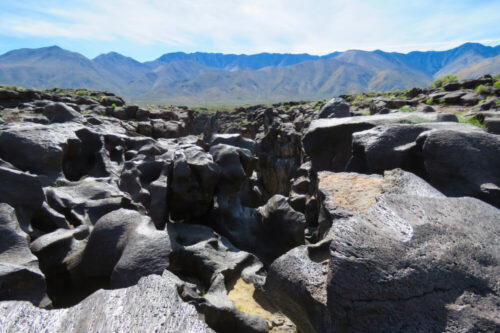 Rocky terrain with large cracks and crevices, set against a backdrop of mountain range under a bright, clear sky. visit bishop