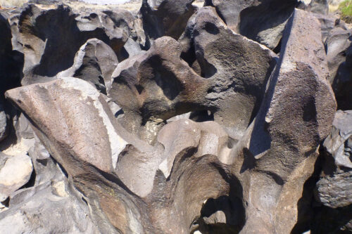 A cluster of jagged volcanic rock formations in an arid landscape with clear skies. visit bishop