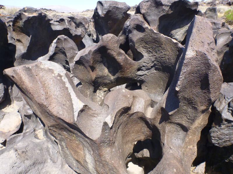 A cluster of jagged volcanic rock formations in an arid landscape with clear skies. visit bishop