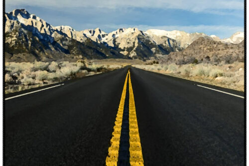 Empty road with yellow lines leading to a snowy mountain range under a blue sky with light clouds. visit bishop