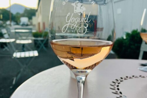 A glass of wine on an outdoor table at sunset in Bishop, California, with "Good Earth Yogurt Wine Bar" printed on the glass. visit bishop