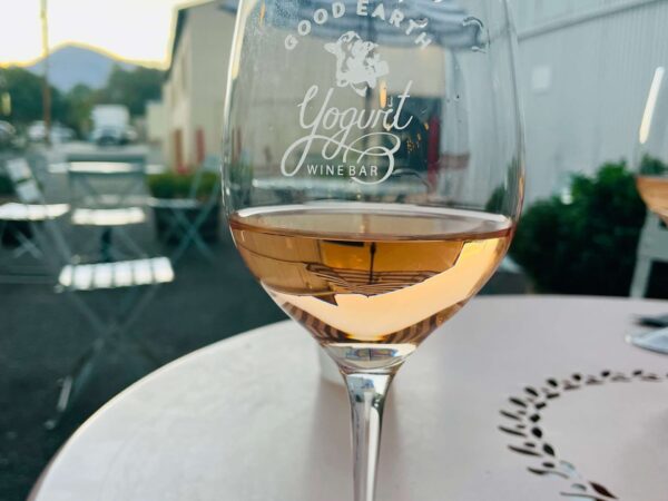 A glass of wine on an outdoor table at sunset in Bishop, California, with "Good Earth Yogurt Wine Bar" printed on the glass. visit bishop