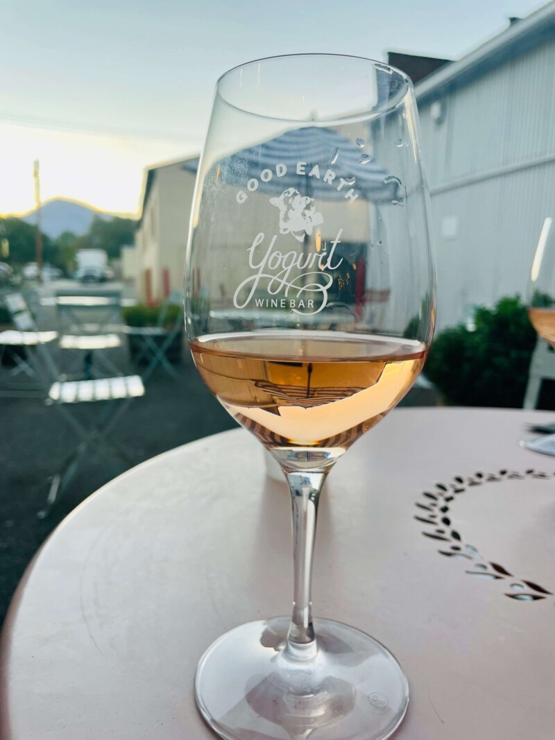 A glass of wine on an outdoor table at sunset in Bishop, California, with "Good Earth Yogurt Wine Bar" printed on the glass. visit bishop