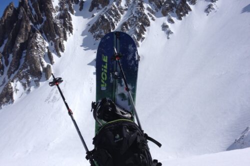 Backpack with skis and poles positioned upright in the snow, with a rugged, snow-covered mountain in the background. visit bishop