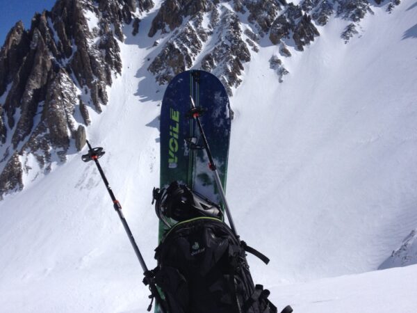 Backpack with skis and poles positioned upright in the snow, with a rugged, snow-covered mountain in the background. visit bishop