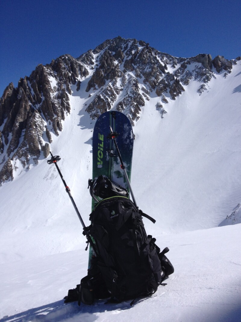 Backpack with skis and poles positioned upright in the snow, with a rugged, snow-covered mountain in the background. visit bishop