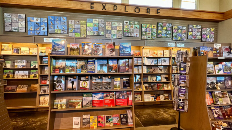 Bookshelf with various travel guides, maps, and nature guides, beneath a sign that reads "EXPLORE" and a colorful mural. visit bishop