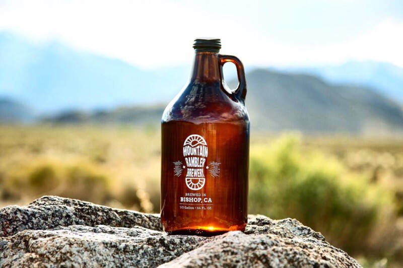 A brown glass jug with a Mountain Rambler Brewery label sits on a boulder in a mountainous landscape. visit bishop