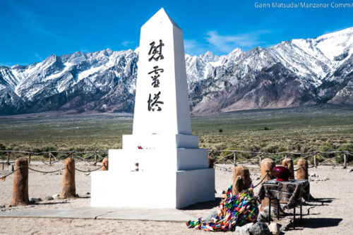 A white obelisk monument, inscribed with Japanese characters, stands before snow-capped mountains. visit bishop