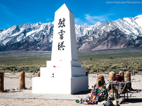 A white obelisk monument, inscribed with Japanese characters, stands before snow-capped mountains. visit bishop