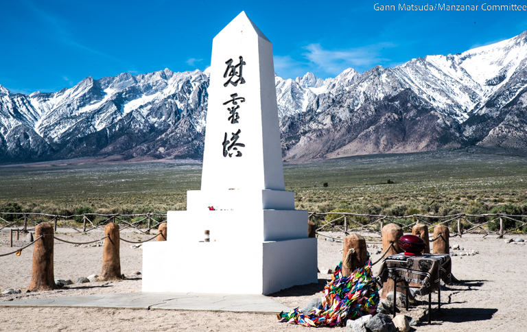 A white obelisk monument, inscribed with Japanese characters, stands before snow-capped mountains. visit bishop