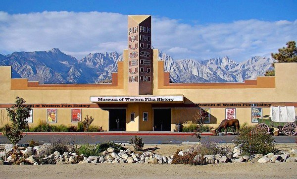 A tan building with a "Museum" sign, mountain backdrop, posters, a horse, and a wagon in front. Text: "Museum of Western Film History" in Bishop, California's Eastern Sierra. visit bishop