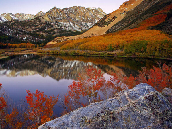 Mountain landscape with a calm lake reflecting autumn foliage and snow-capped peaks under a clear sky. visit bishop