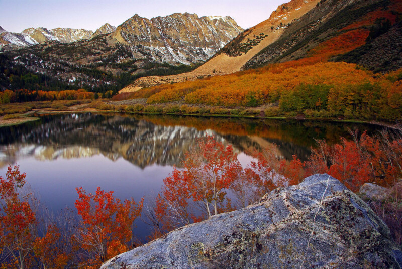 Mountain landscape with a calm lake reflecting autumn foliage and snow-capped peaks under a clear sky. visit bishop