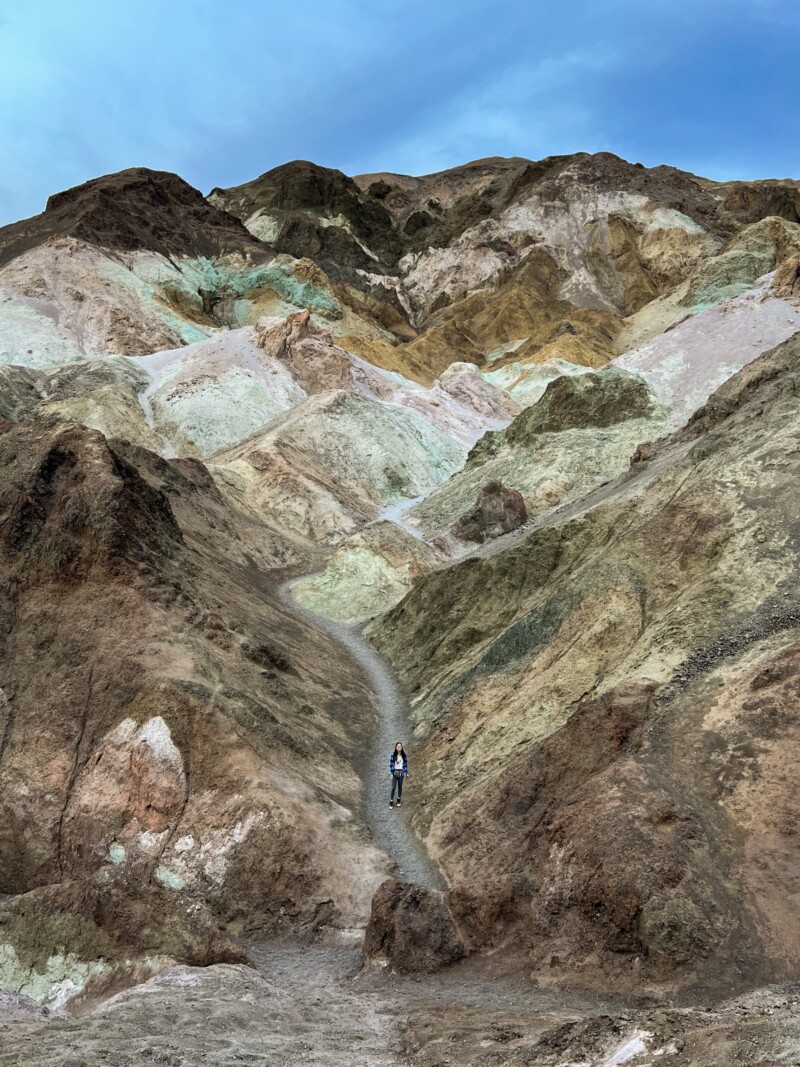 A person walks a narrow path in a colorful, rocky landscape under a blue sky. visit bishop