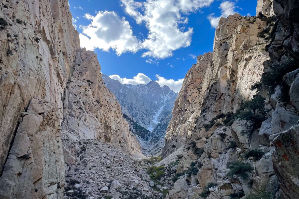 A rugged canyon with steep rock walls, loose boulders, and a clear blue sky with scattered clouds above. visit bishop