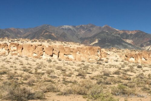 Rock formations and sparse vegetation in a desert landscape with mountains under a clear blue sky in the background. visit bishop