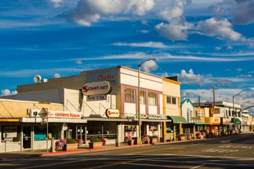 A small-town main street with various shops and businesses under a partly cloudy sky. visit bishop