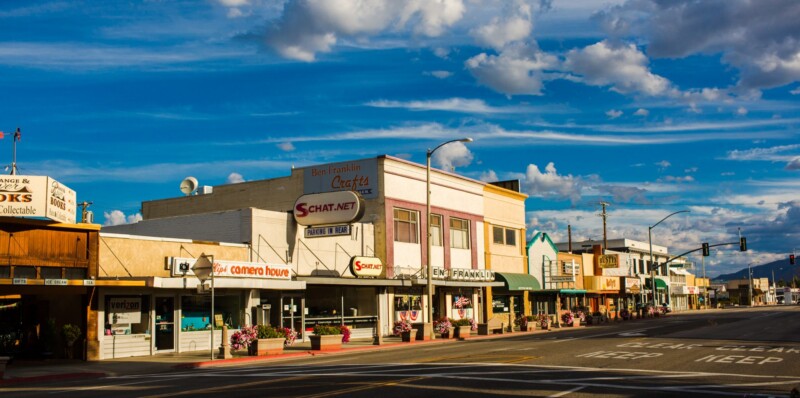 A small-town main street with various shops and businesses under a partly cloudy sky. visit bishop