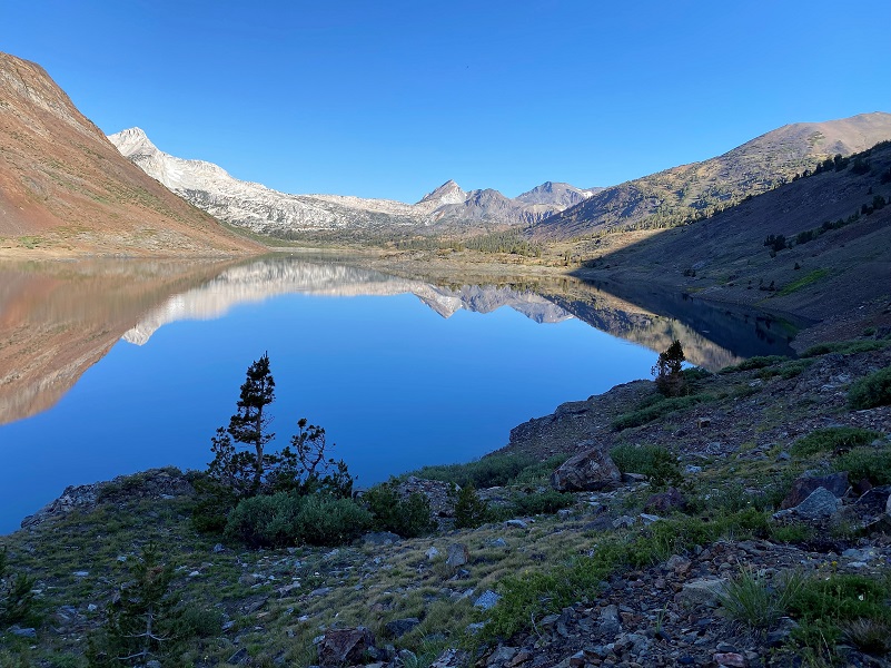 A serene mountain lake with clear blue water, reflecting surrounding peaks, under a bright blue sky. visit bishop