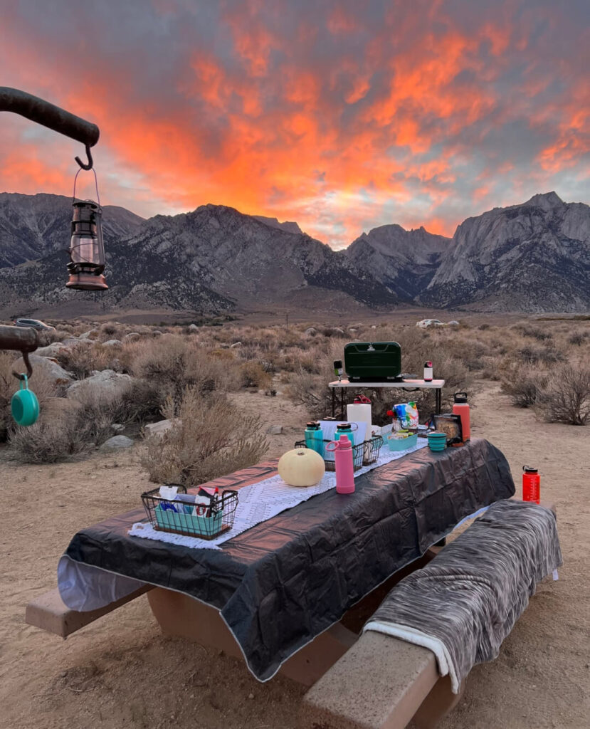 A campsite with a picnic table set for dinner, mountains in the background, and a colorful sunset sky in the breathtaking Eastern Sierra near Bishop, California. visit bishop