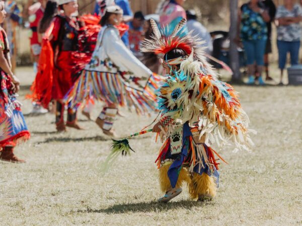 People in colorful traditional attire dancing outside on a grassy area in Bishop, California, with spectators in the background. visit bishop