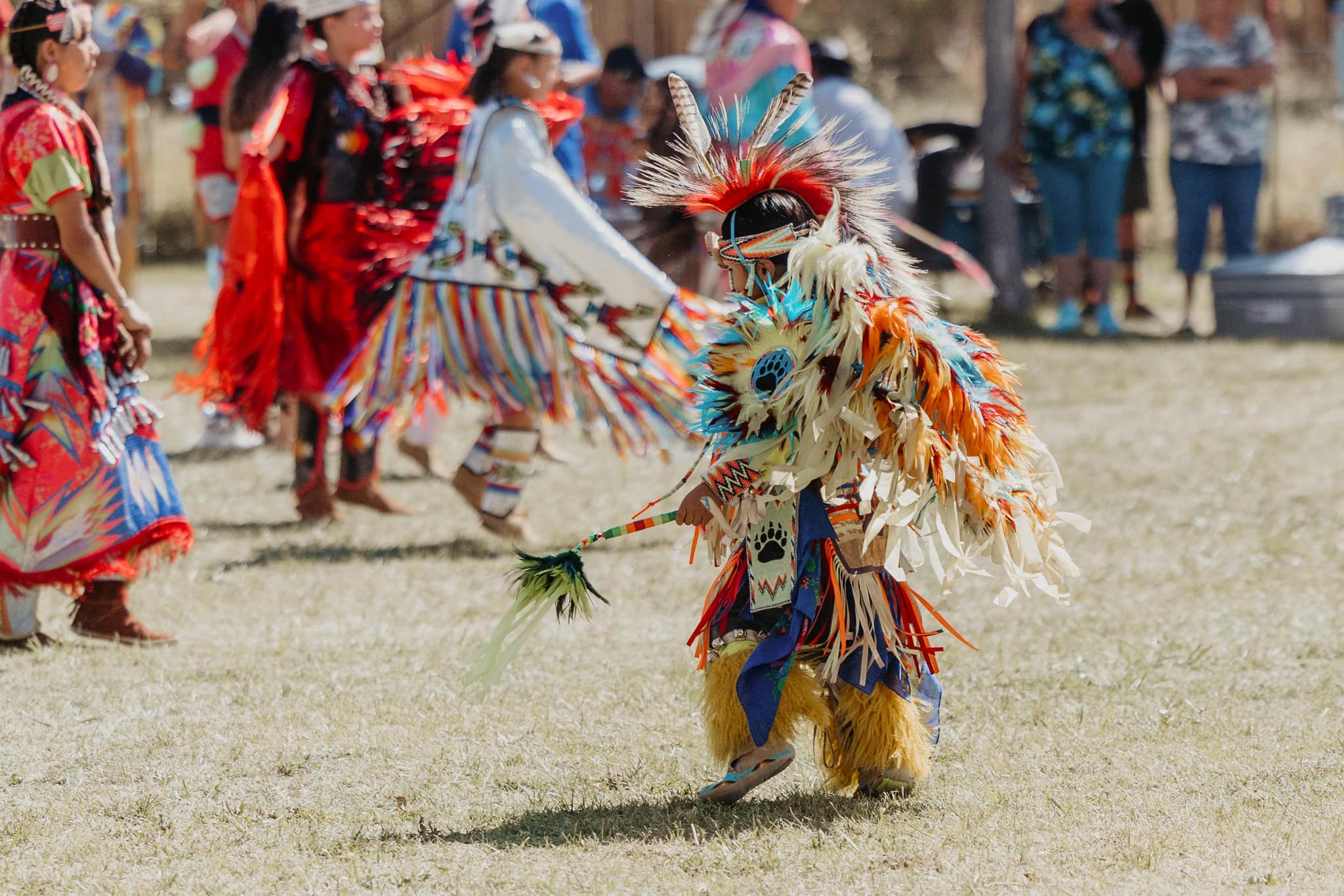 People in colorful traditional attire dancing outside on a grassy area in Bishop, California, with spectators in the background. visit bishop