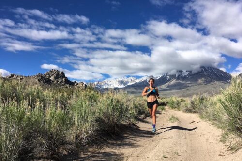 A person running on a trail in the mountainous landscape of Bishop, California, under a blue sky with clouds, capturing the essence of the stunning Eastern Sierra scenery. visit bishop