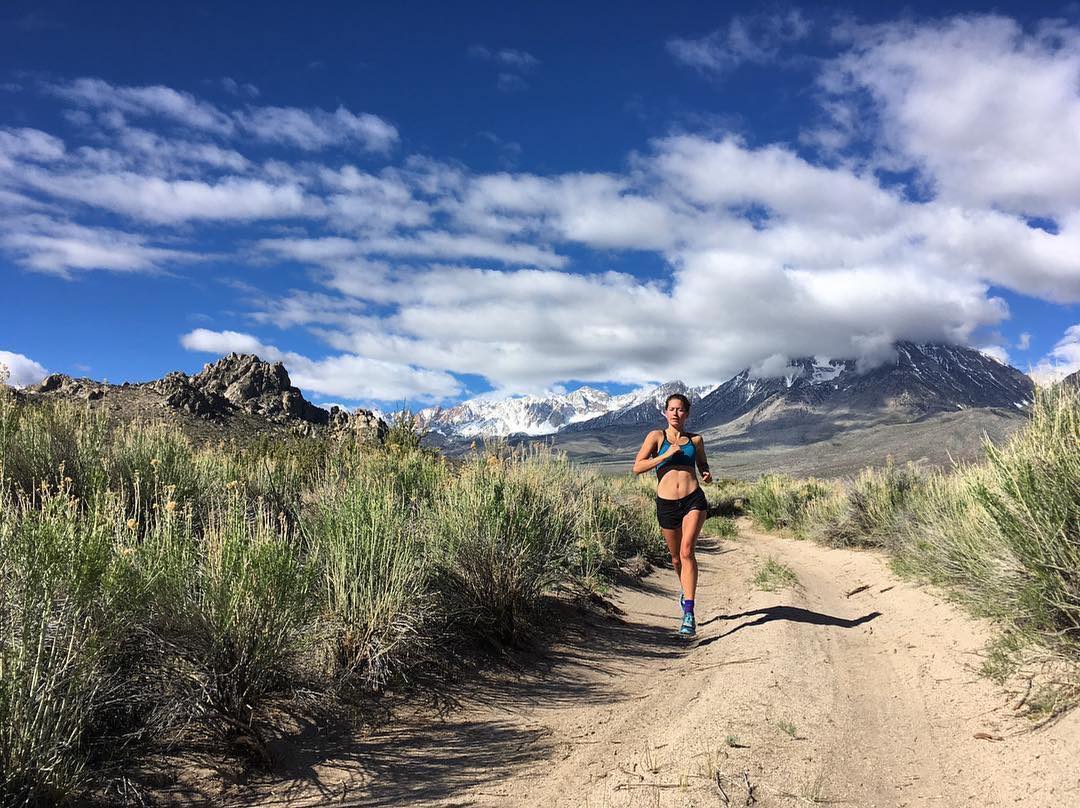 A person running on a trail in the mountainous landscape of Bishop, California, under a blue sky with clouds, capturing the essence of the stunning Eastern Sierra scenery. visit bishop