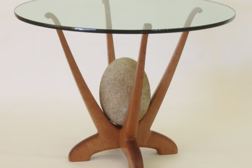 Glass-top table with uniquely designed wooden legs, featuring a centered decorative stone. visit bishop