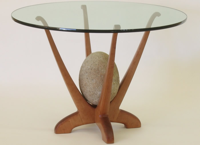 Glass-top table with uniquely designed wooden legs, featuring a centered decorative stone. visit bishop