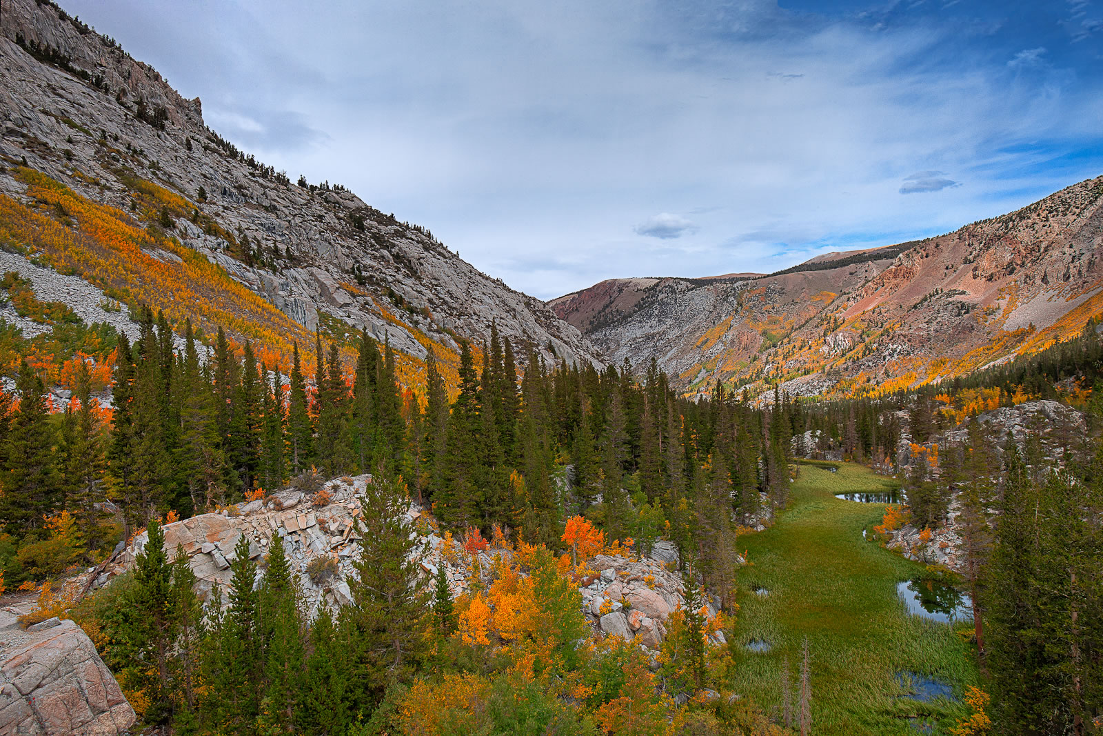 Mountain landscape in Bishop, California with autumn trees in vibrant colors, a lush green meadow under the clear blue sky with clouds; the Eastern Sierra provides a breathtaking backdrop. visit bishop