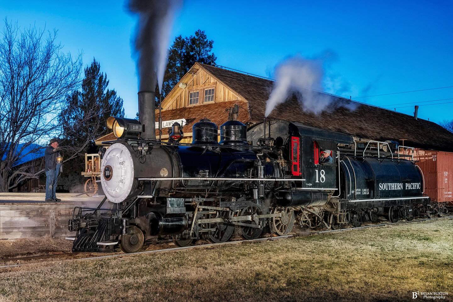 Black steam locomotive labeled "Southern Pacific 18" emits steam near a wooden building at dusk in Bishop, California. visit bishop