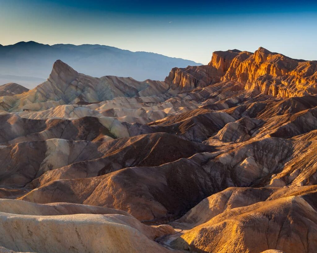 Mountain range with rugged, layered rocky terrain under a clear blue sky during sunset or sunrise, nestled in the heart of Bishop, California's Eastern Sierra. visit bishop