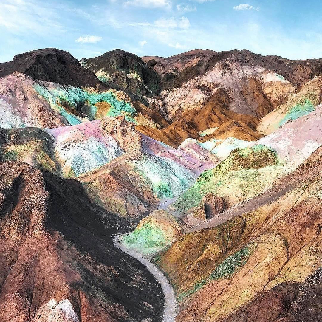 Multicolored mountain range with hues of teal, yellow, brown, and pink under a partly cloudy sky in the Eastern Sierra near Bishop, California. visit bishop